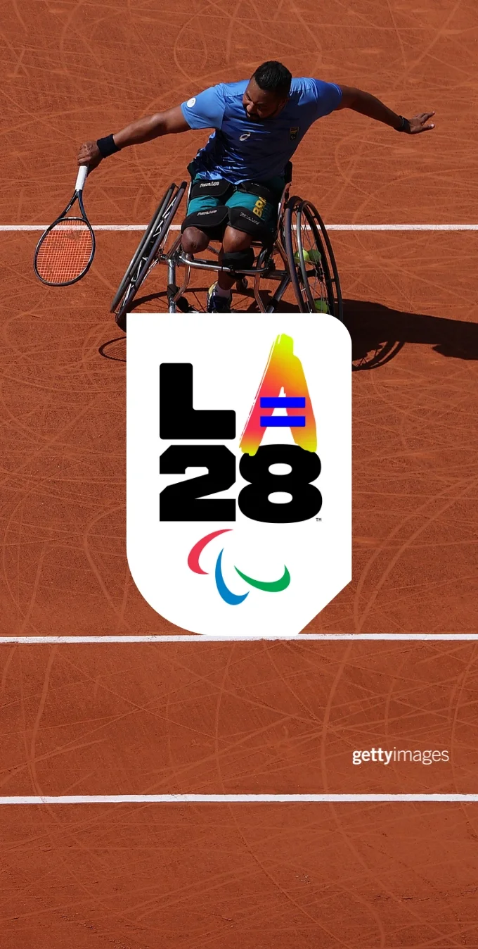 Photograph of a Paralympian tennis player holds a tennis raquet while a tennis ball is in the air while playing on a tennis court. The LA28 Paralympic Equality 'A' is overlayed on top of the photograph.