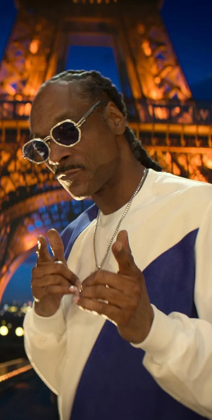 Una imagen mostrando a Snoop Dogg apuntando a la cámara con la Torre Eiffel de fondo.