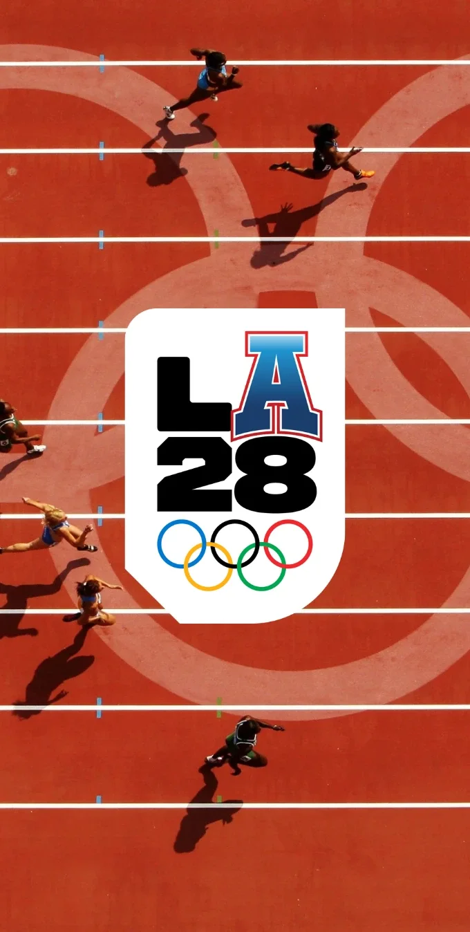 Overhead photograph of Olympic track athletes running on a red track with the Olympic rings logo on the track. The LA28 Varsity A emblem is overlayed on top of the photograph.