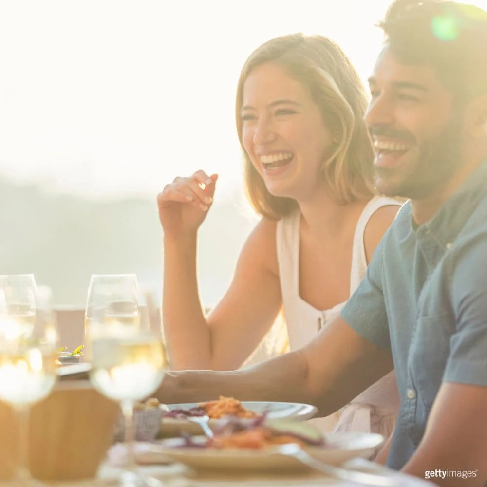 Fotografía de una mujer y un hombre sentados juntos en una mesa sonriendo mientras beben vino.