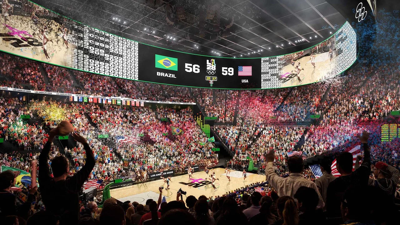 Una representación digital muestra un concurrido partido de baloncesto en la Olympic and Paralympic Arena, también conocida como el Intuit Dome. El marcador muestra USA 59 y Brasil 56, y las grandes pantallas digitales que rodean la cancha muestran la acción del juego. El estadio está lleno de aficionados emocionados con banderas de varios países. La cancha tiene el logotipo de LA28, indicando que es un juego olímpico. Hay muchas luces coloridas y confeti en la escena.