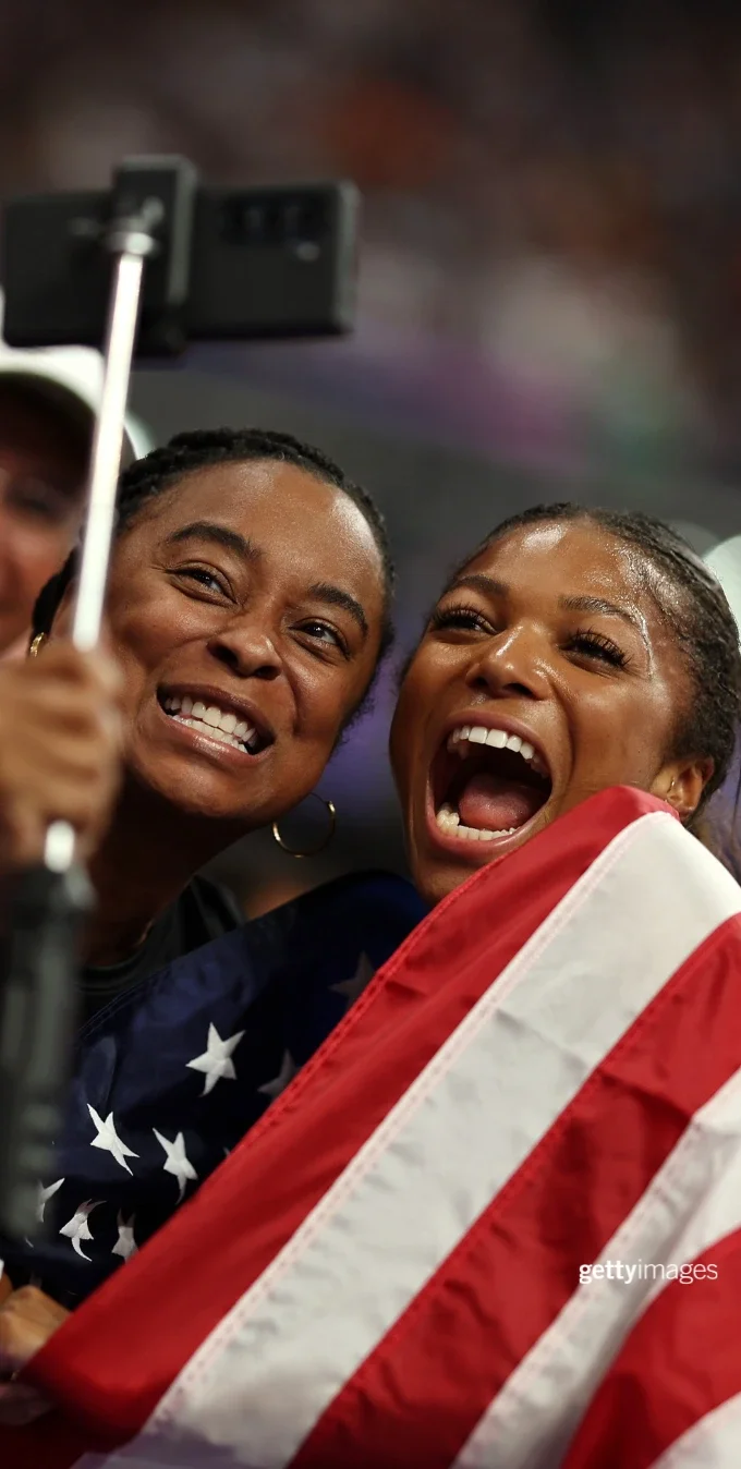 Olympian Gabby Thomas celebrating with fans while wrapped in an American flag at the Paris 2024 Olympics. 