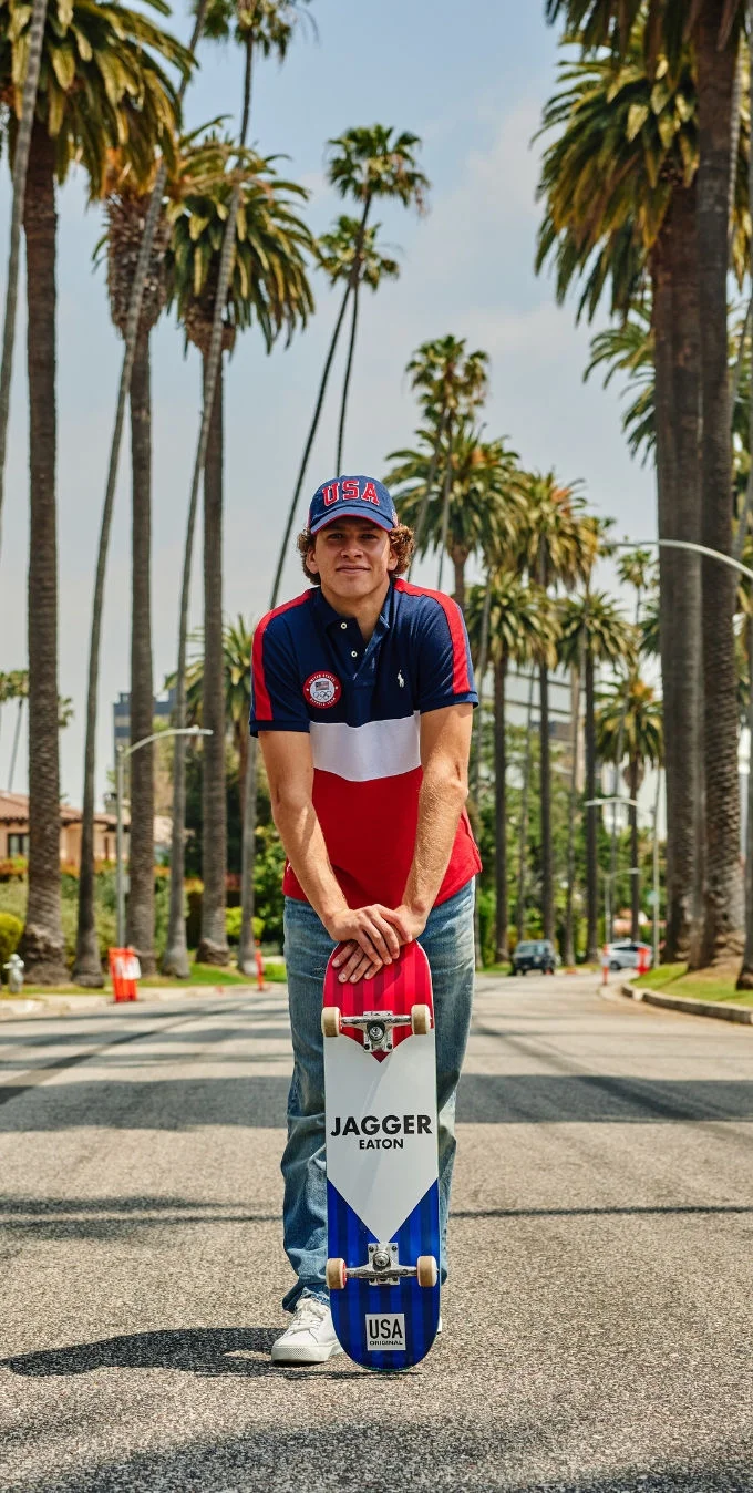 Jagger Eaton standing with a Team USA skateboard on a residential street in Los Angeles while wearing a Ralph Lauren Olympic Polo and jeans. 